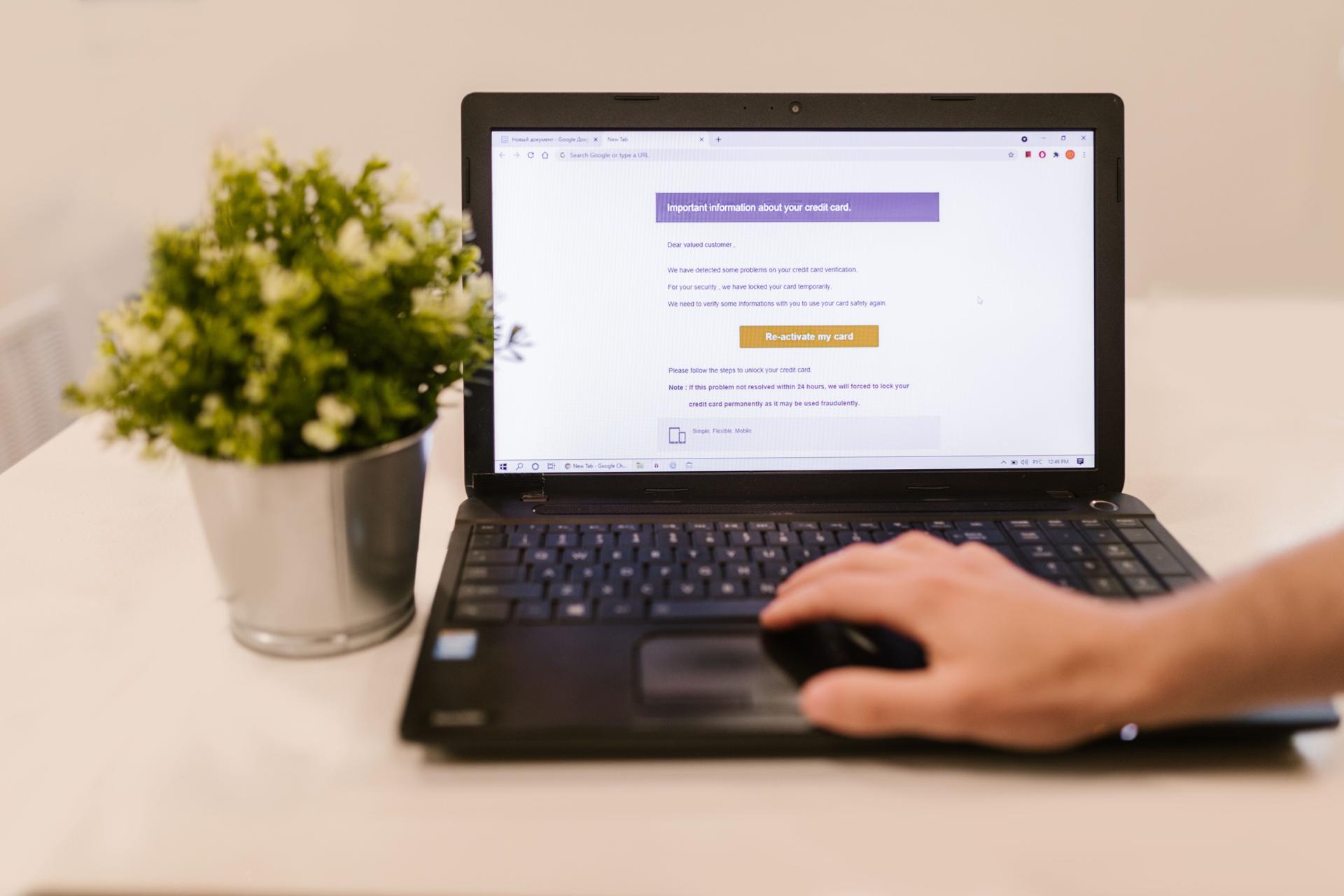 A laptop displaying an unexpected credit-card reactivation message while a person uses the trackpad